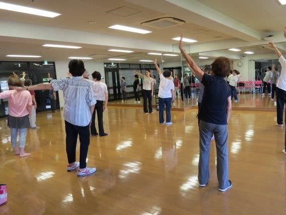 大きな鏡張りの部屋でみんなで体操をする様子