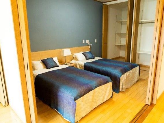 寝室は焦げ茶色と白の壁でシックな印象である。ベッドの間には間接照明が置いてある。ベッドは２つあり、それぞれ枕が３つ置いてある。