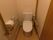 白をメインとした、シンプルなトイレが設置されている。便座のすぐとなりに可動式の手すりを設置。壁側にもＬ字形の手すりを備えつけてある。