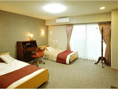 白いシーツが整えられた、茶のアクセントがホテルのような印象を与えるベッドが２台置かれている。窓の横にはポールハンガーも置いてある。