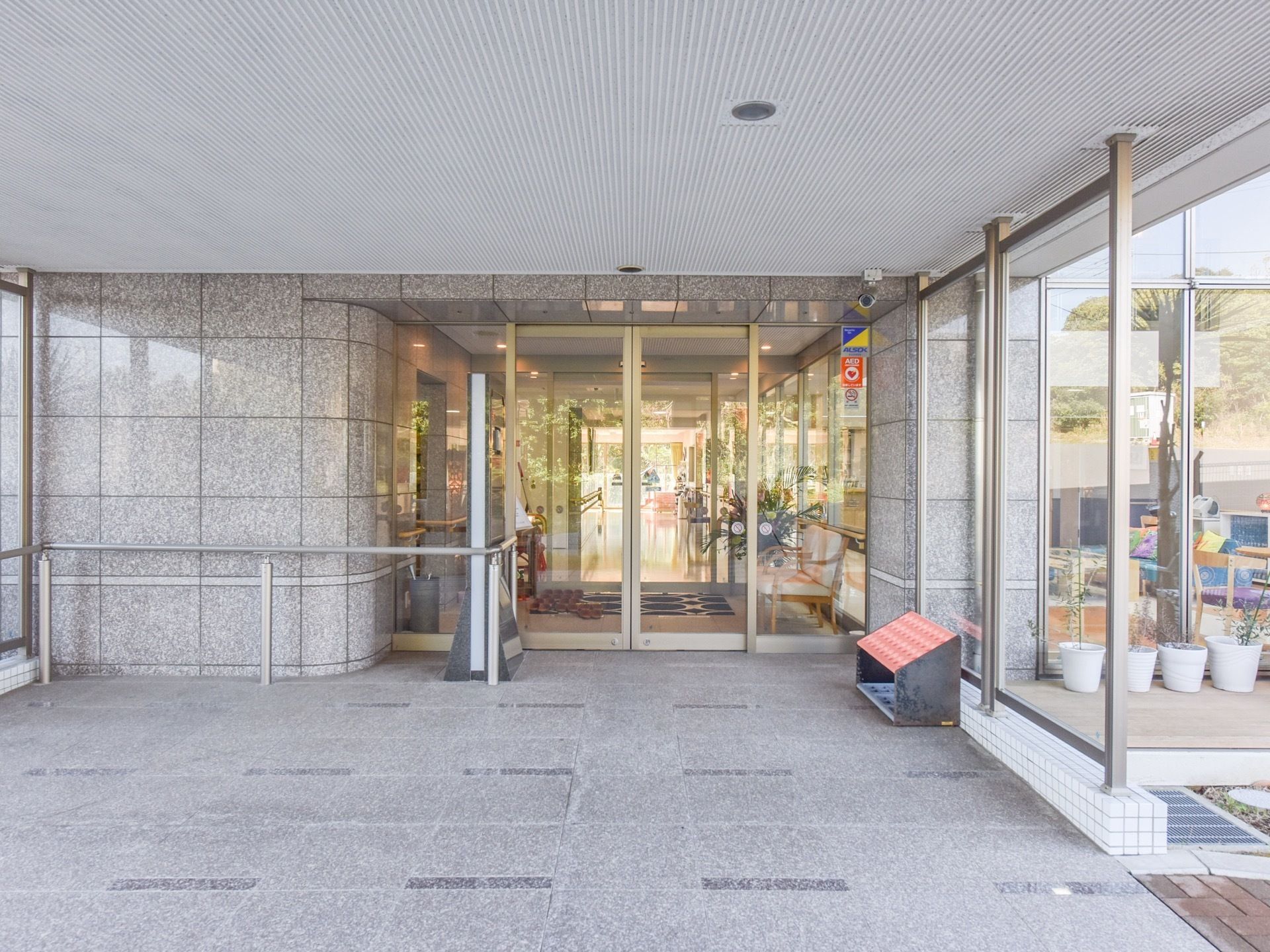 玄関正面からの写真。扉は自動ドアで建物内の見通しが良い。壁には手すりが設置されている。入り口には傘立てがある。