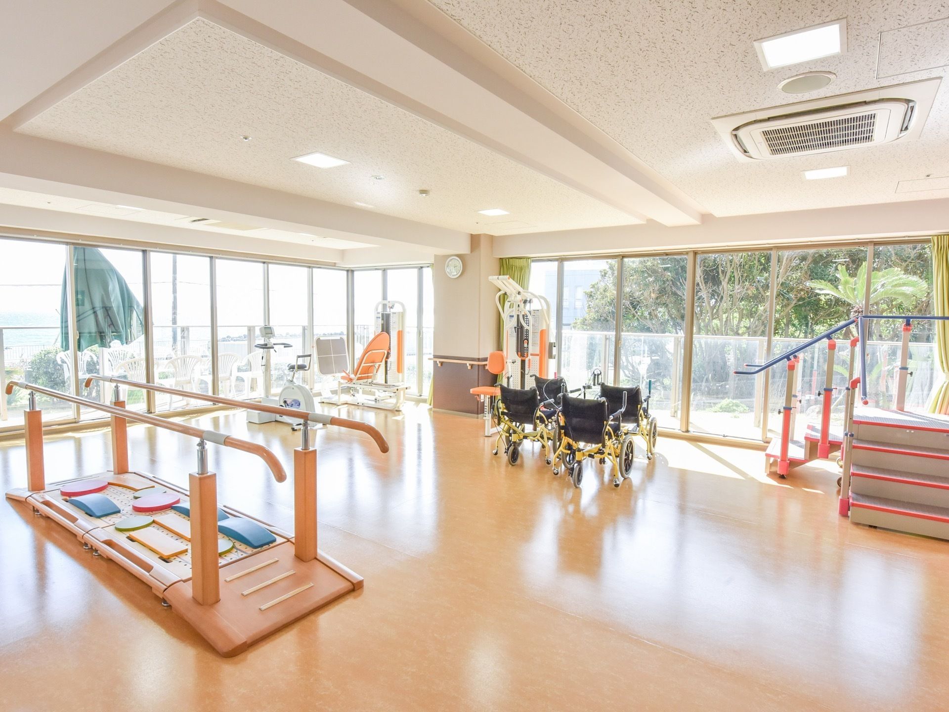 訓練用階段、平行棒、エアロバイク、滑車運動器などさまざまなリハビリ器具がある。窓は全面ガラスで広く明るい空間。