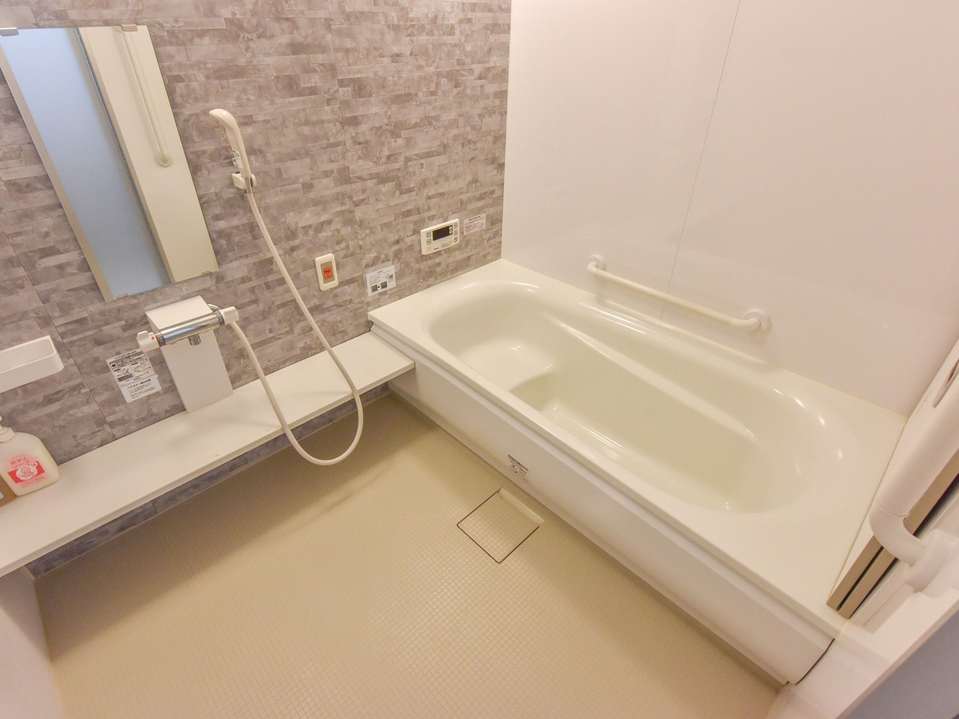 壁の一部はグレーで白を基調とした清潔な浴室である。シャワーと鏡、非常ボタンが設置されている。浴槽には手すりがついている。