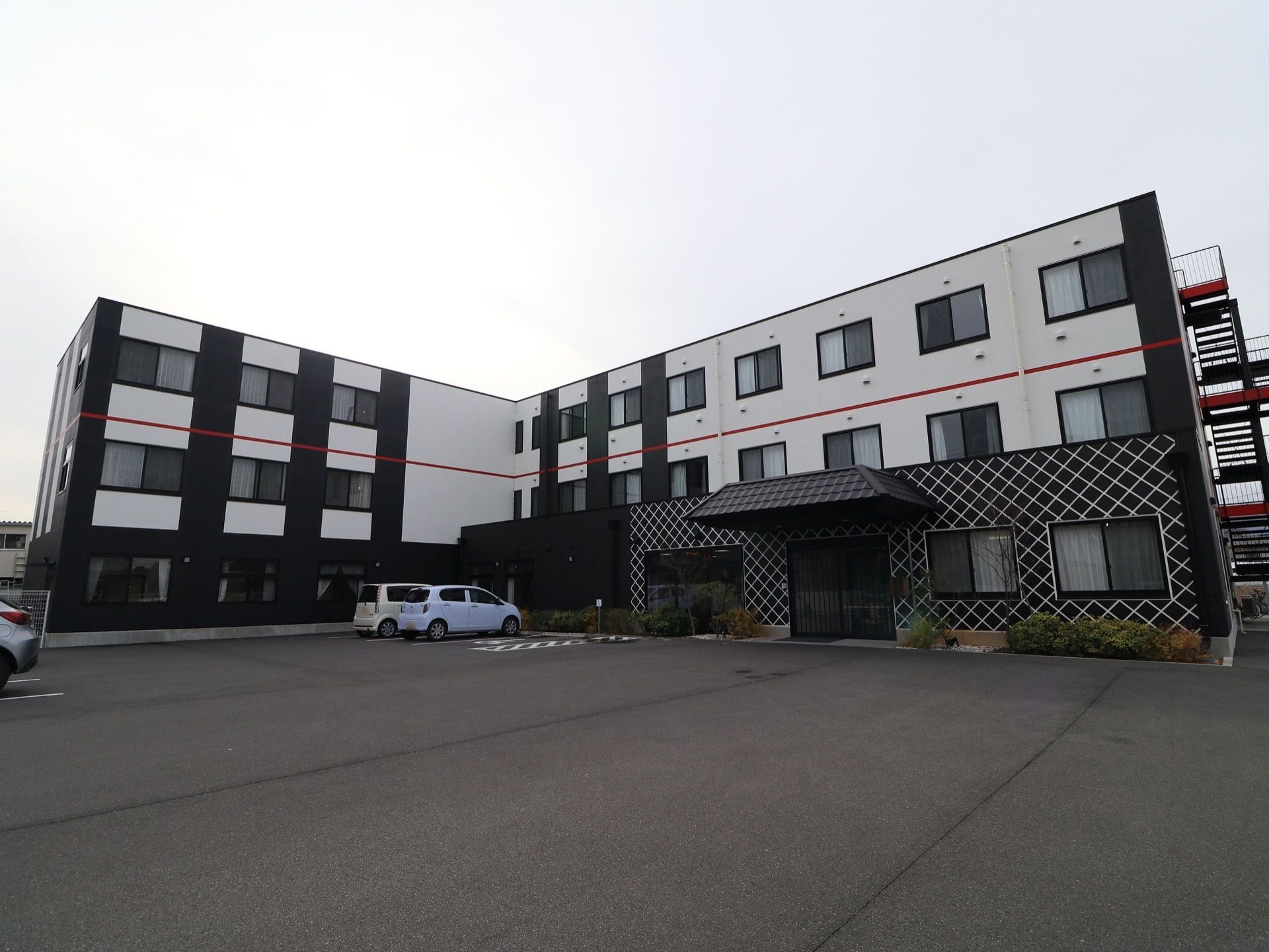 白と黒のモダンなデザインの施設である。３階建てになっており、非常階段が設置されている。建物前には、駐車場が設けられている。