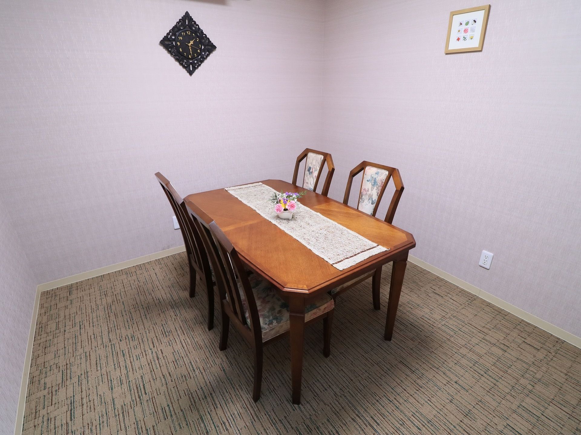相談室はラベンダー色の壁紙が印象的な部屋である。４人掛けテーブルが置かれている。デザイン性の高い時計が壁に設置されている。