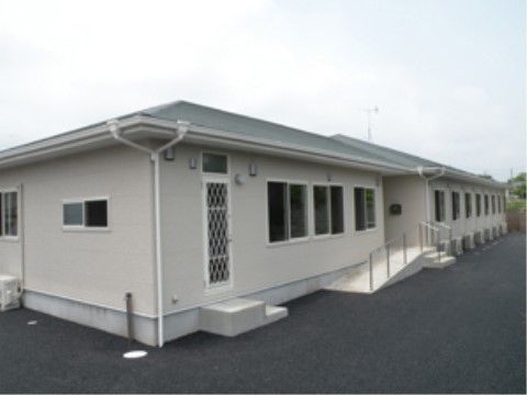 落ち着いた色合いの平屋建ての施設。車椅子が通れるスロープがある。建物の周りには、障害となるものおかれていない。