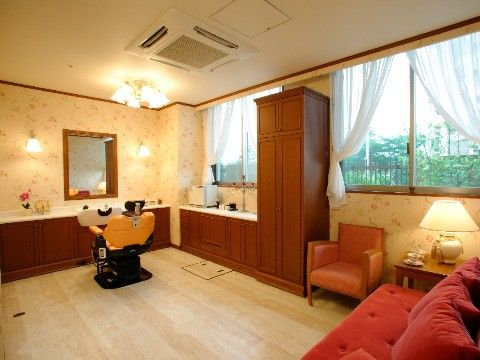 ビューティサロンには家具が配置されている。腰高窓にはレースのカーテンが掛かっている。手前には赤いソファがある。