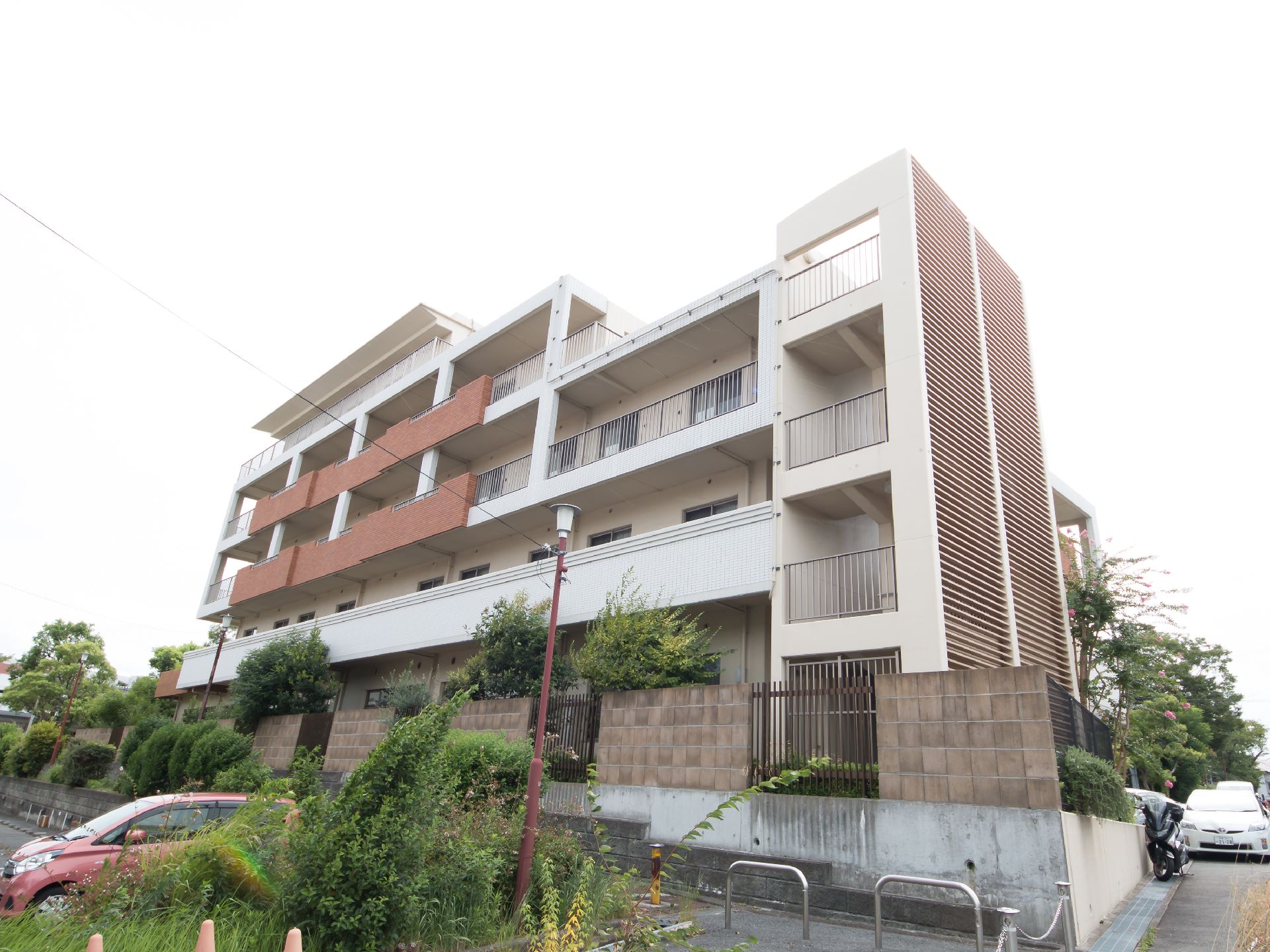 塀や緑に一面を囲まれている、外階段付きの四階建て施設外観