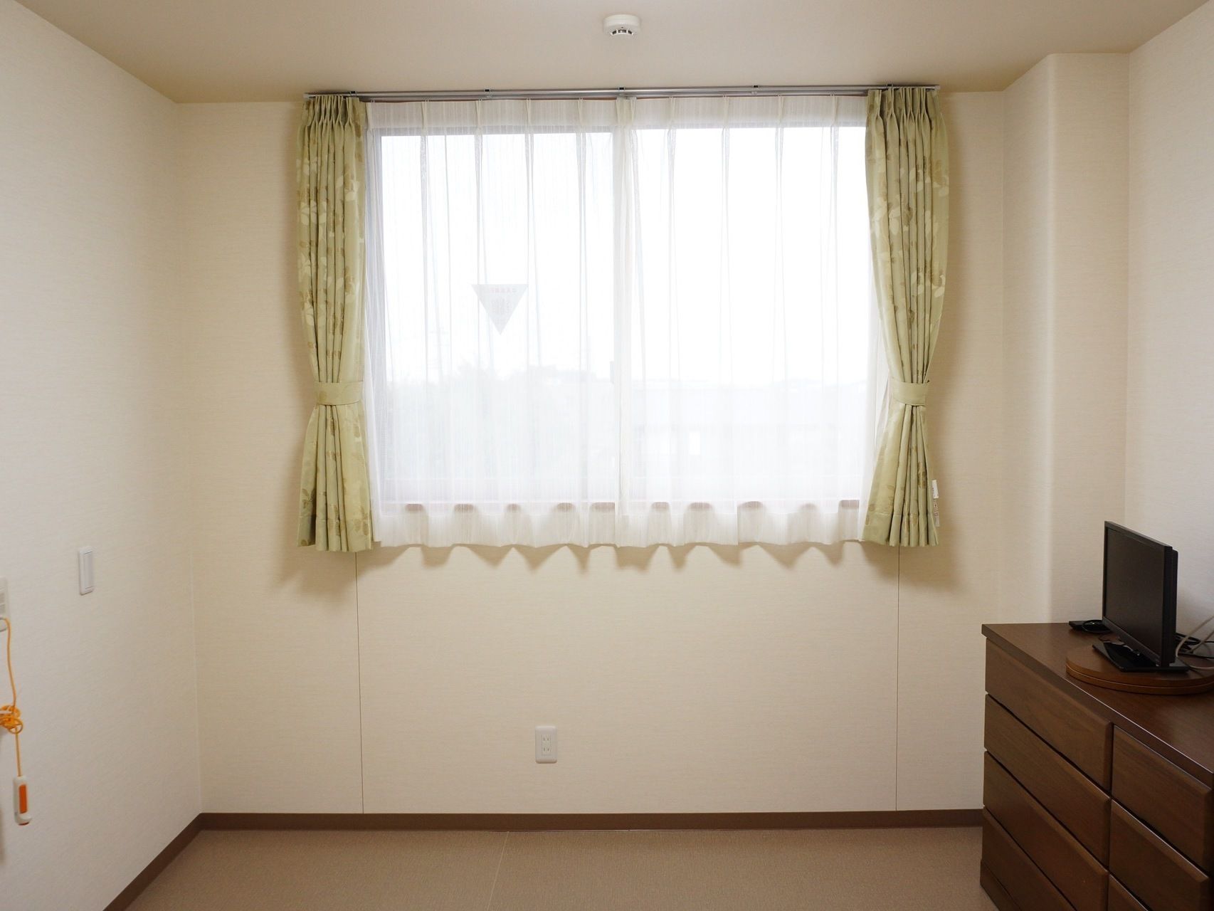 居室にはレースとまとめられたカーテンが掛かった窓がある。窓には消防隊侵入口となる下三角マークが印されている。