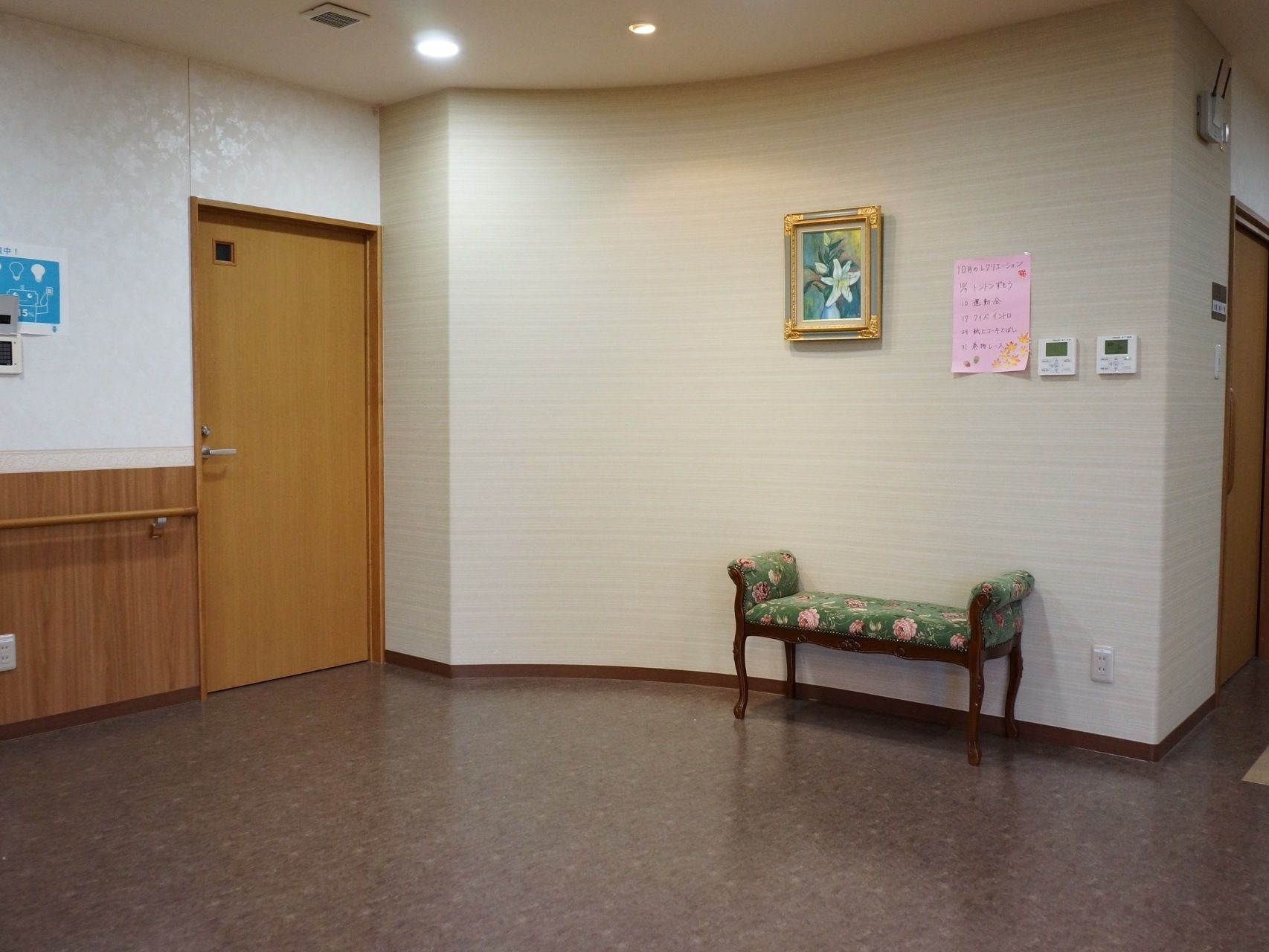 10月のリクリエーション活動の予定が書かれた紙が通路の壁側に貼られている。下には花柄の椅子が置かれている。