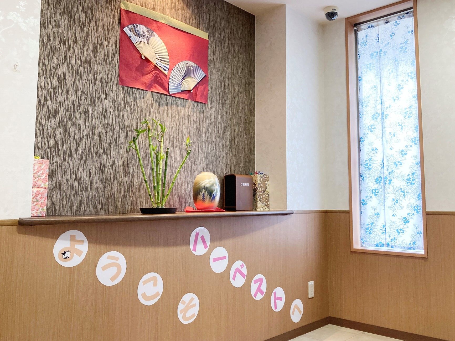さまざまな花がダイナミックに飾られた花瓶がライトアップされているエントランス。縦長の窓から日差しも入っている。