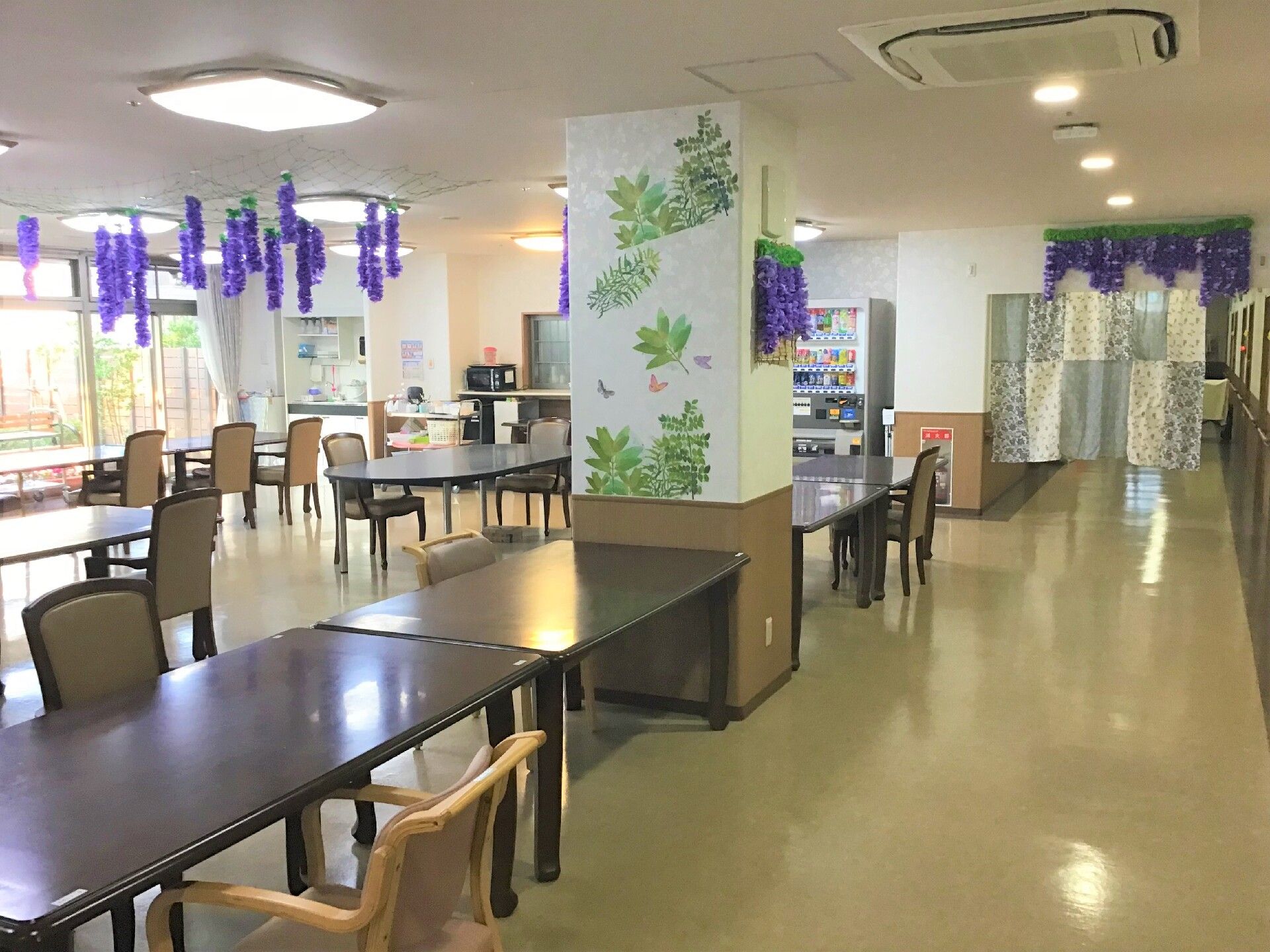 食堂には茶色いテーブルと背もたれとひじ掛け付きの椅子が並んでいる。各テーブルにはチラシで作った箱が置かれている。