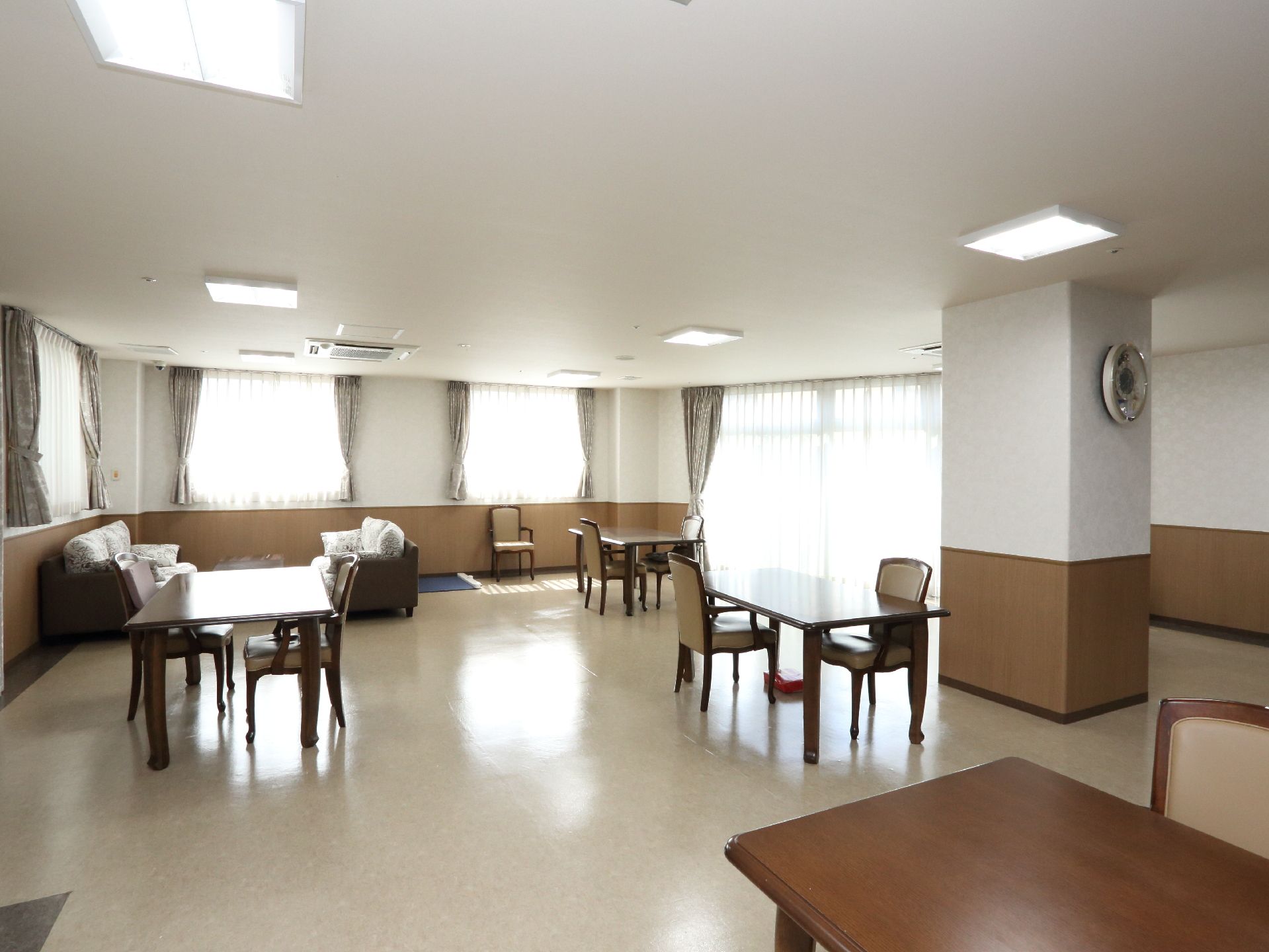 広々とした空間には茶色いテーブルが4台、椅子が7脚置かれている。壁側には椅子1脚とソファーが2つ置かれている。