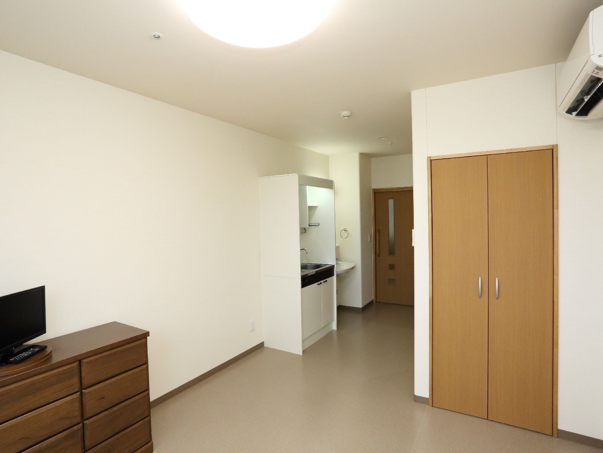 ダークブラウンの箪笥の上にはテレビが置かれている。部屋にはキッチンもあり、両開きのクローゼットも備え付けられている。