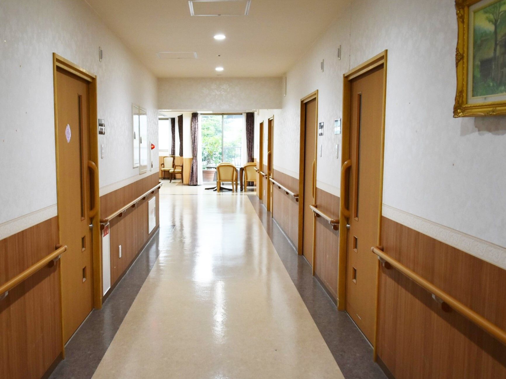 白色と黒色の2色の床の廊下には入居者の個室がずらりと並んでいる。部屋の間には手すりが設置されている。