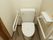 白い壁のスペースに洋式便器が置かれたトイレがある。便器の両側には手すりがあり、壁側には呼び出しボタンも設置されている。