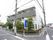 白と黒を基調とした３階建ての建物である。建物の周囲には植物が多く植えられていて、木の横に青い看板がある。