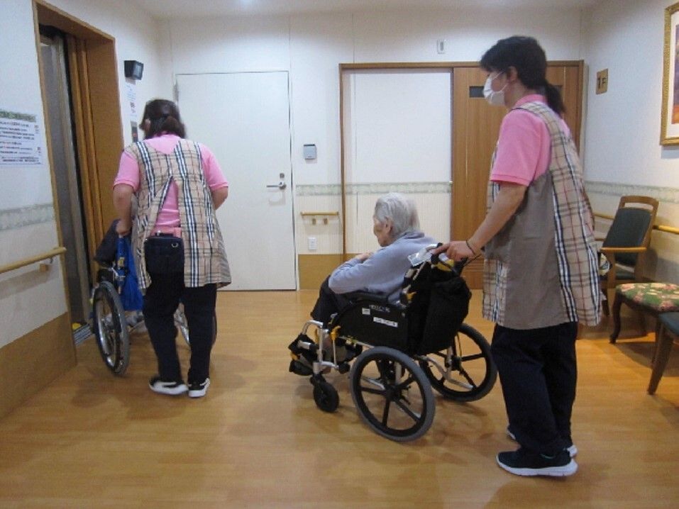 車椅子に座っている高齢女性と寄り添う男性ヘルパー
