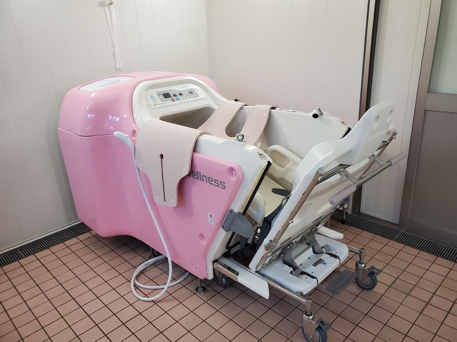 ピンクの機会浴槽。床は茶のタイル張り。使いやすそうなデザインである。