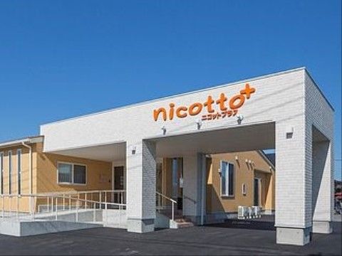 ツートンカラーの施設の外観。玄関前にはスロープがあり大きな屋根が設けられている。