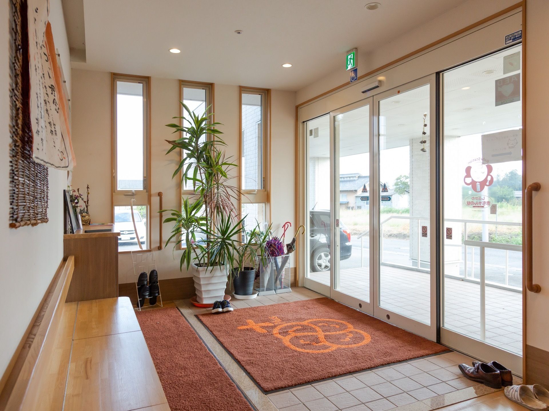 木目調に縁取られた窓がモダンな印象を与える玄関。自動ドアなので、出入りがスムーズに行える。観葉植物が置かれている。