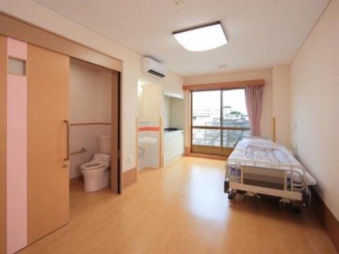居室には、洗面台やトイレ、ミニキッチンなど充実した設備が整えられている。介護ベッドが壁際に置かれている。
