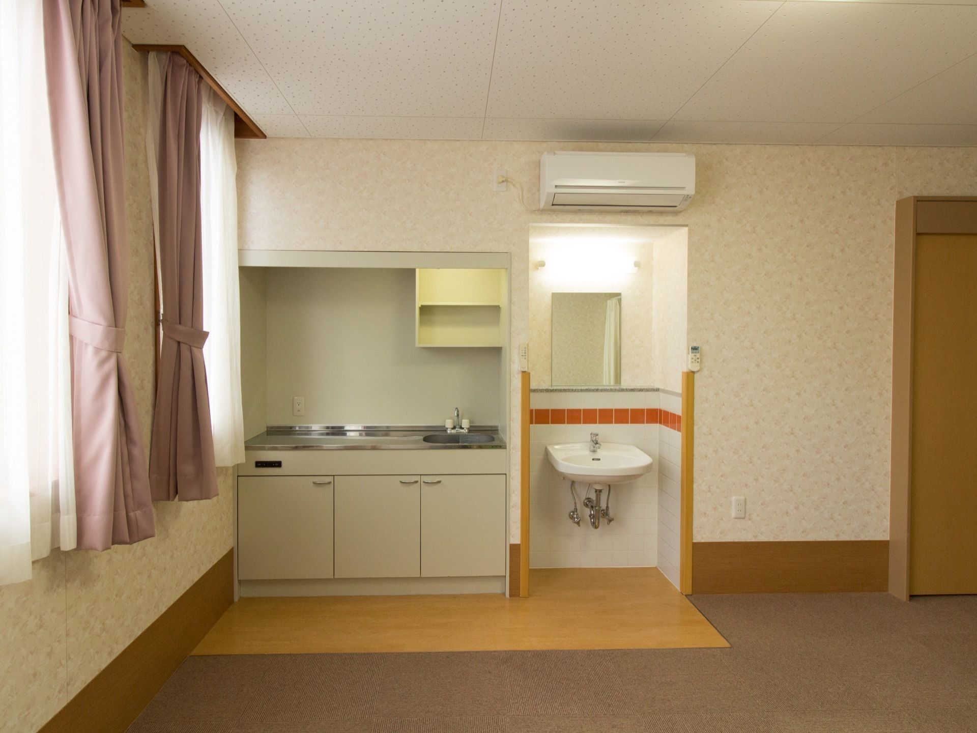 広々とした部屋の隅にコンロのないミニキッチンがあり、そのすぐ隣に鏡とライトの備わった洗面台が設置されている。