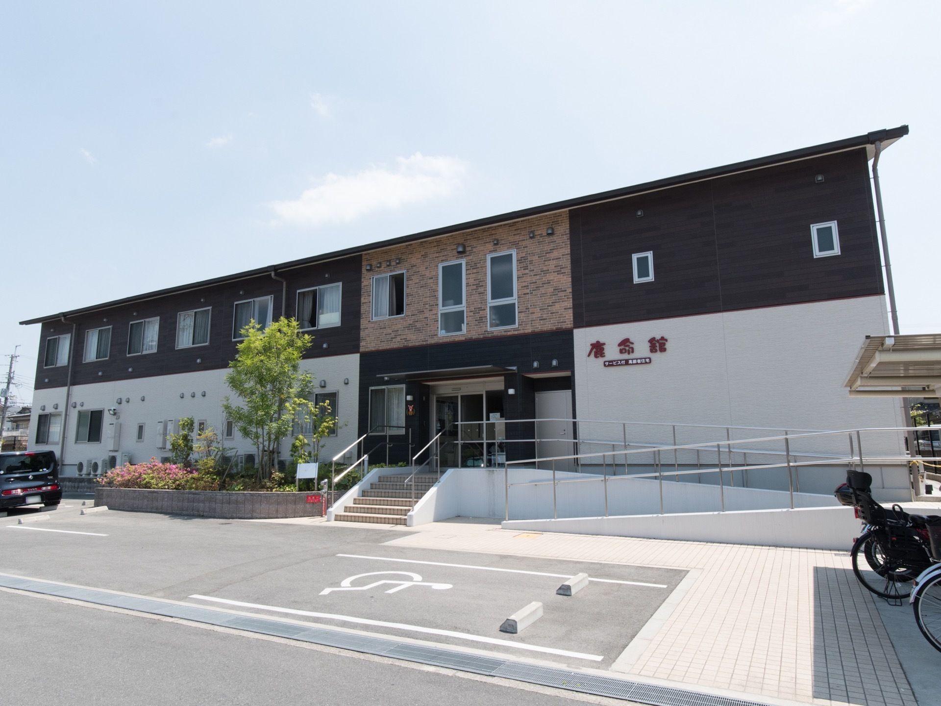 サービス付き高齢者向け住宅は、２階建てである。駐車場や駐輪場が建物前に設けられている。スロープがエントランスに設置されている。