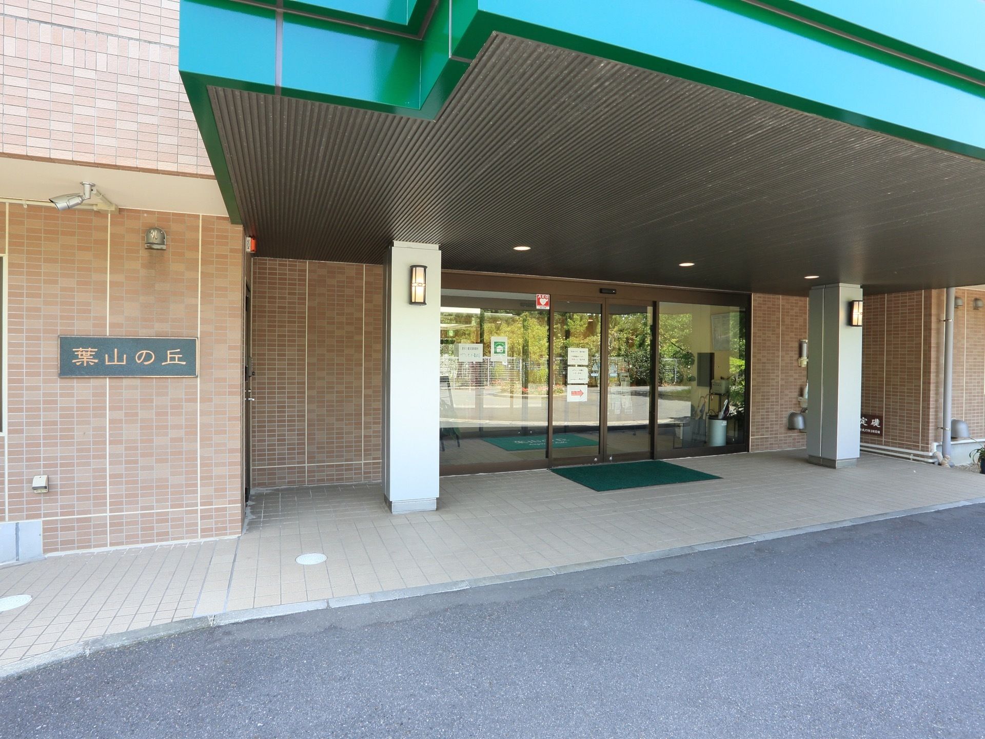 大きな屋根を設けた玄関前は、広々としたスペースを確保している。ガラス張りの自動ドアの傍に玄関マットを敷設している。