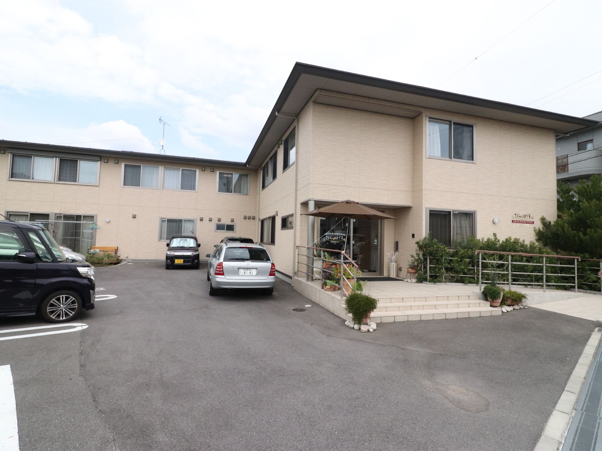 外観は、2階建てのベージュ色をした建物である。駐車場も完備されている。玄関前には、植物が多く植えられている。