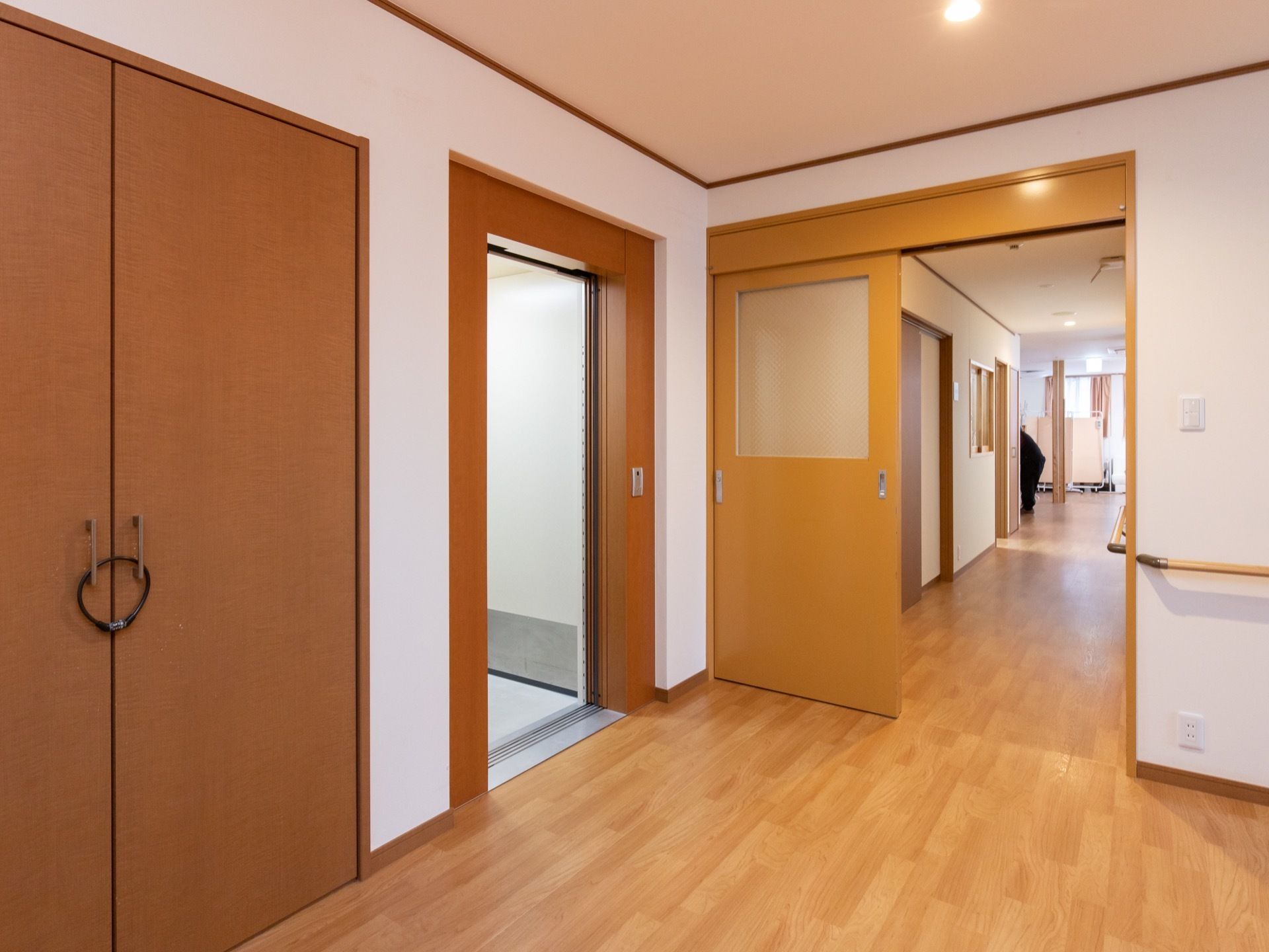 木目のドアで、エレベーターホールは広いスペースが確保されている。エレベーター近くの廊下には、扉がついている。