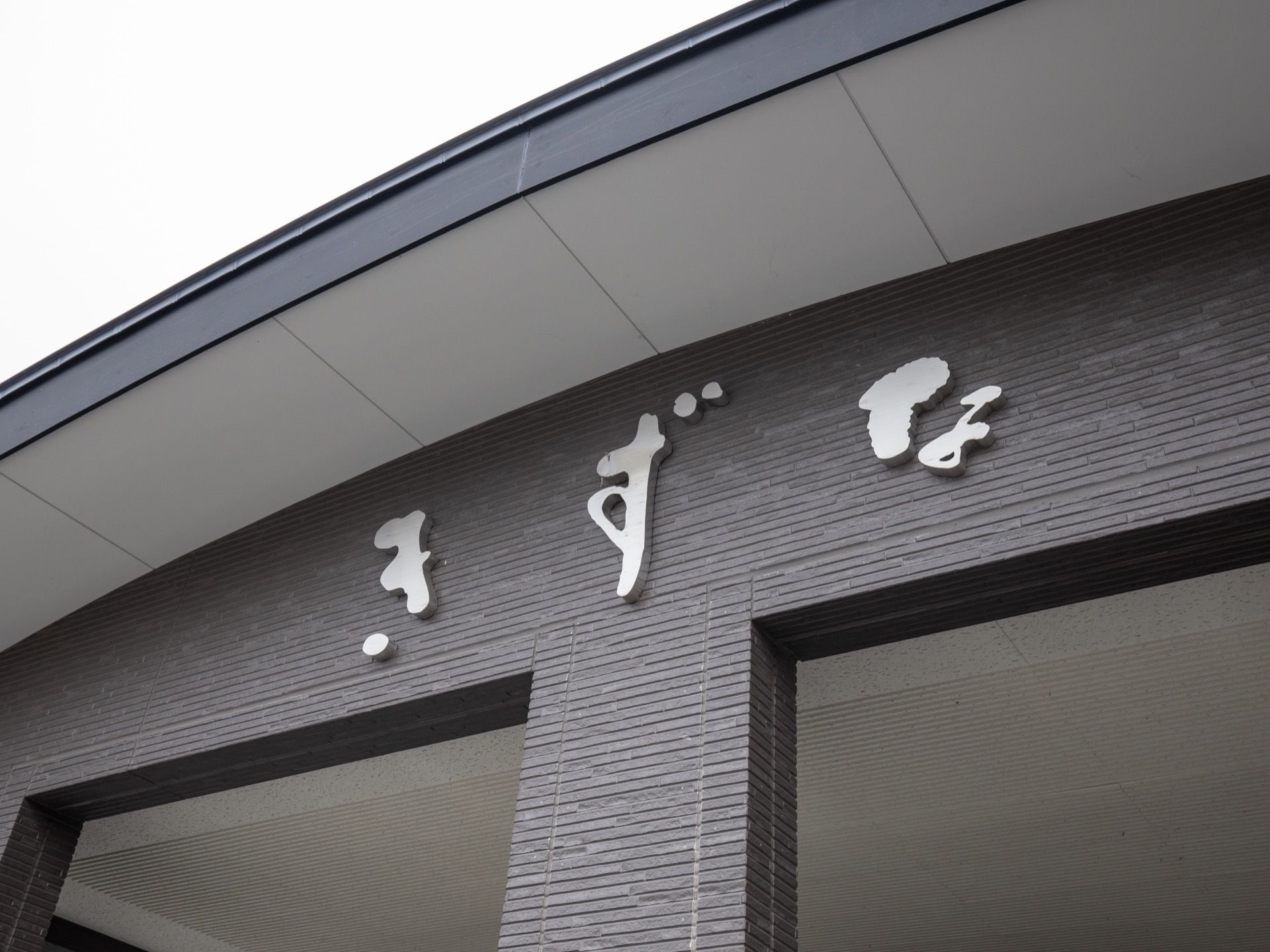 黒い外壁に、銀色の文字で施設名が一文字ずつ書かれている。高い位置に設置されているため、施設名が見えやすい。