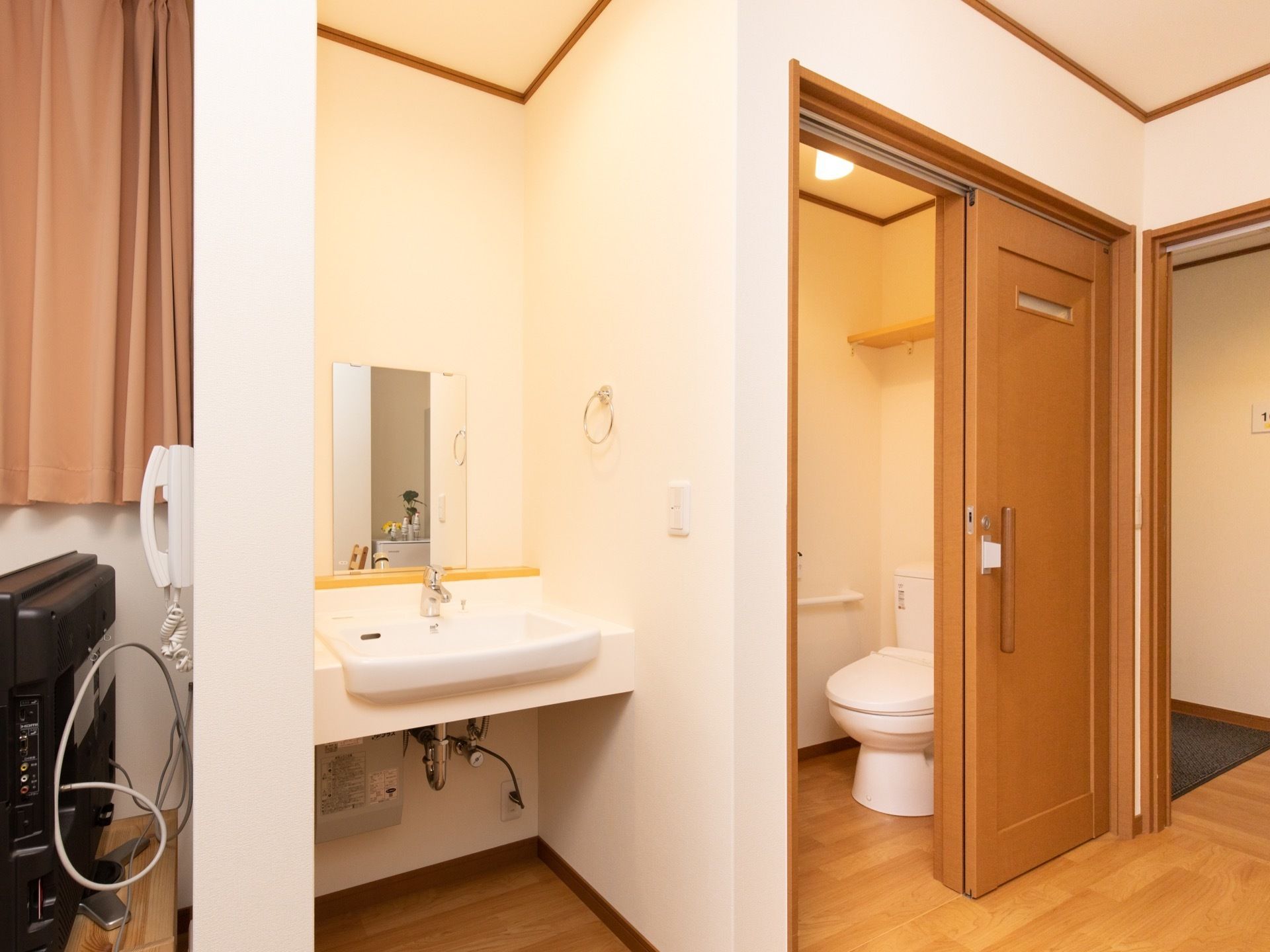 居室内に洗面台を設置しており、壁にはタオルハンガーがある。洗面台の右側にトイレ、左側にテレビが設置されている。