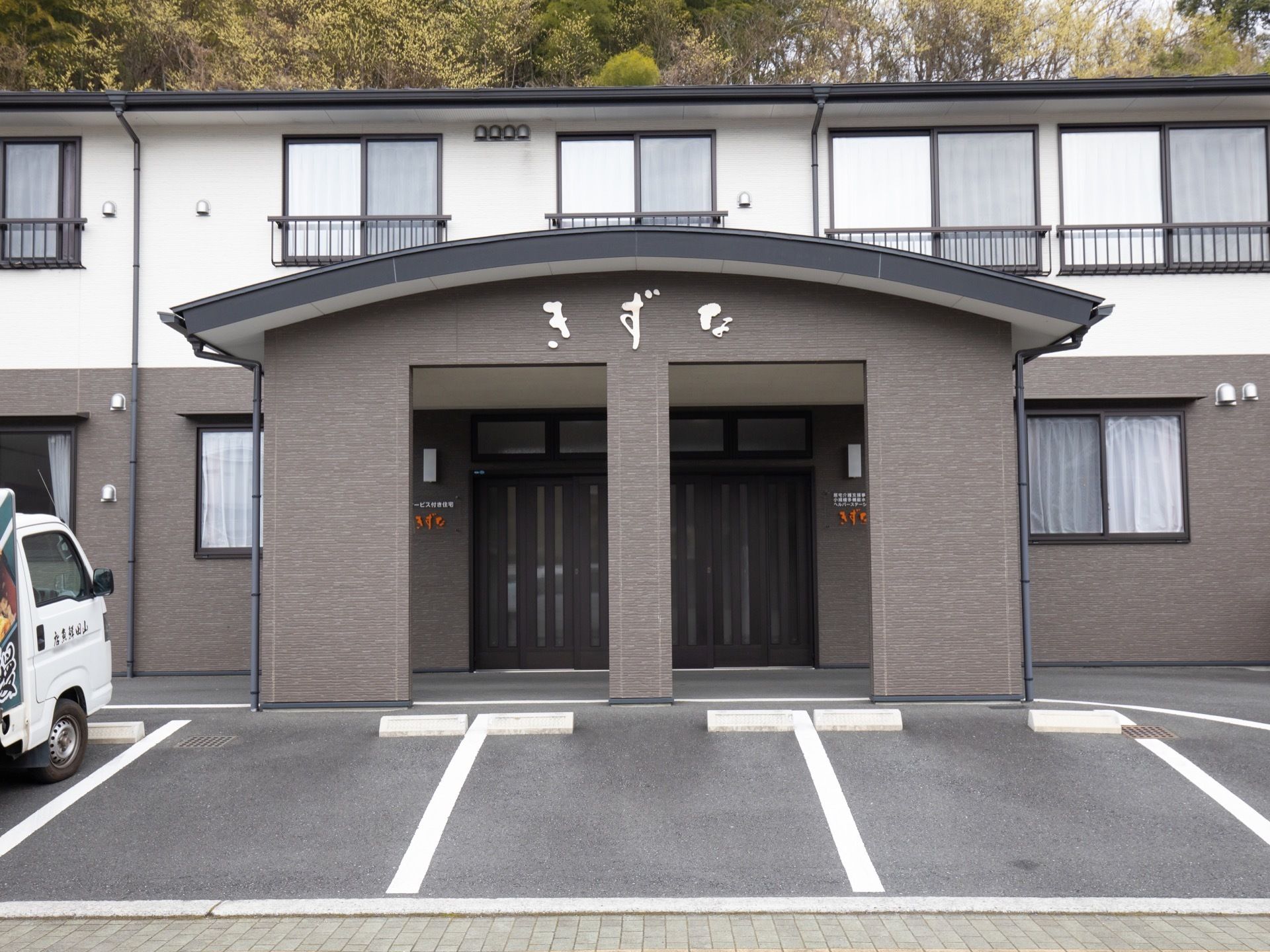 2階建ての建物で、1階部分はグレー、2階部分は白く塗られている。2階の窓には、サッシが取りつけられている。