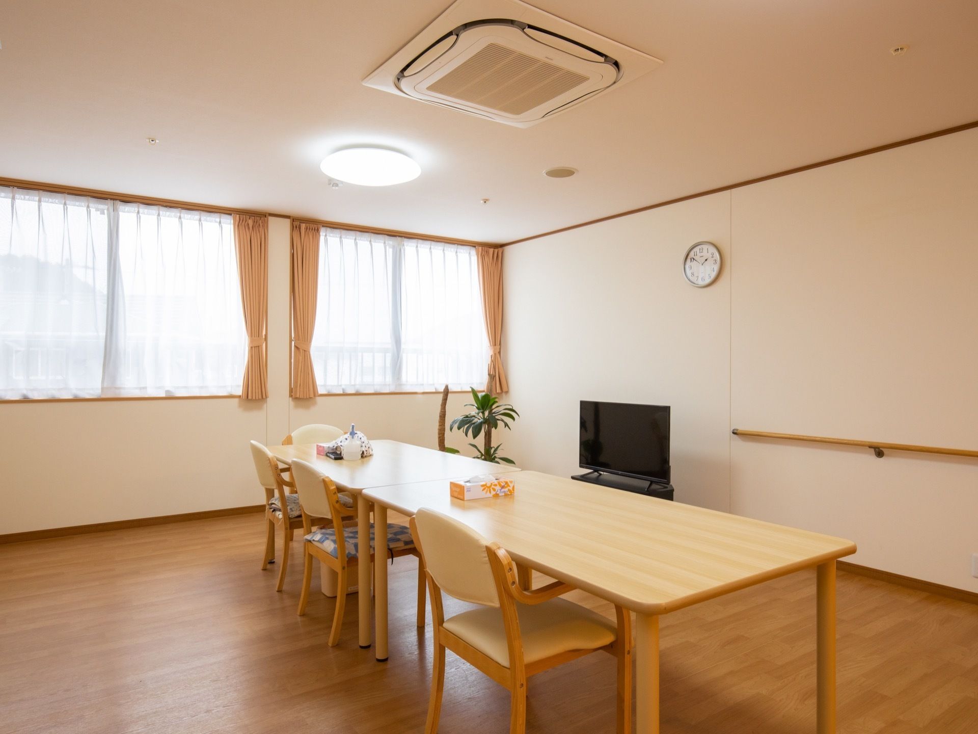 共有スペースは窓に面している。広いスペースにダイニングテーブルが2台並んでいる。壁には手すりが設置されている。