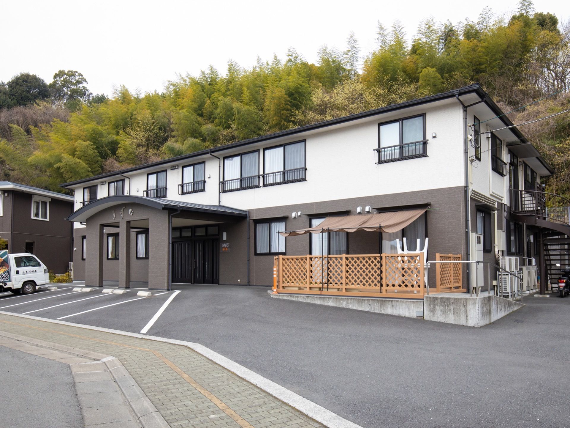 施設は緑豊かな、小高い丘を背に立地している。外壁はブラウンとベージュを使用したスッキリとしたデザインになっている。