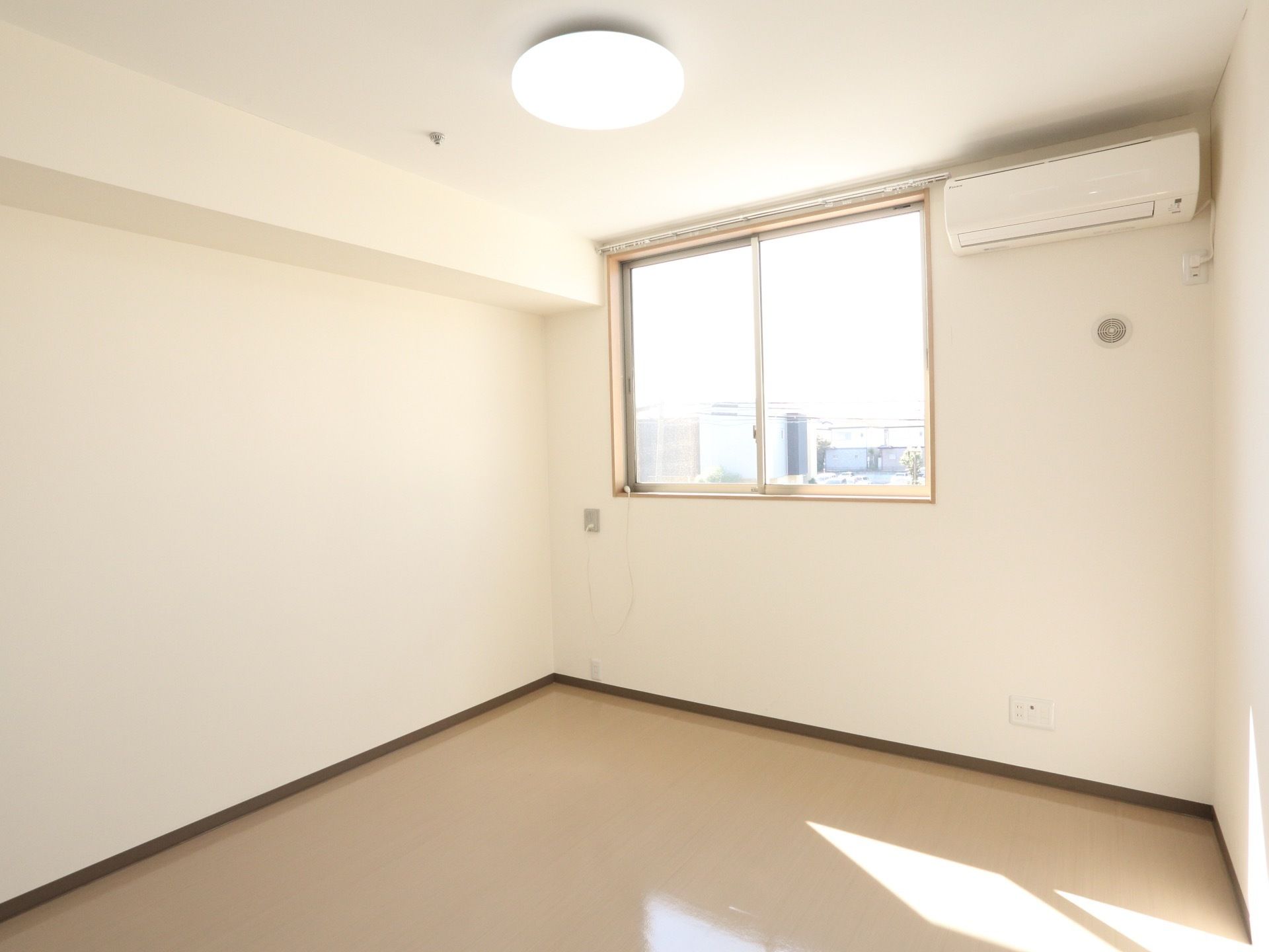 白を基調とした居室には、エアコンと照明器具が取り付けてある。窓は腰高で室内に日差しが差し込んでいる。