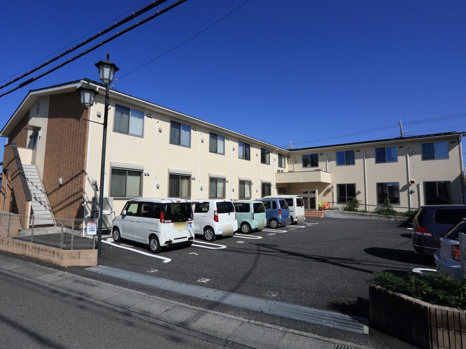 施設は２階建てで、ベージュを基調とした外観に外階段が取り付けられた外壁にブラウンのタイルを貼ったツートンカラーになっている。
