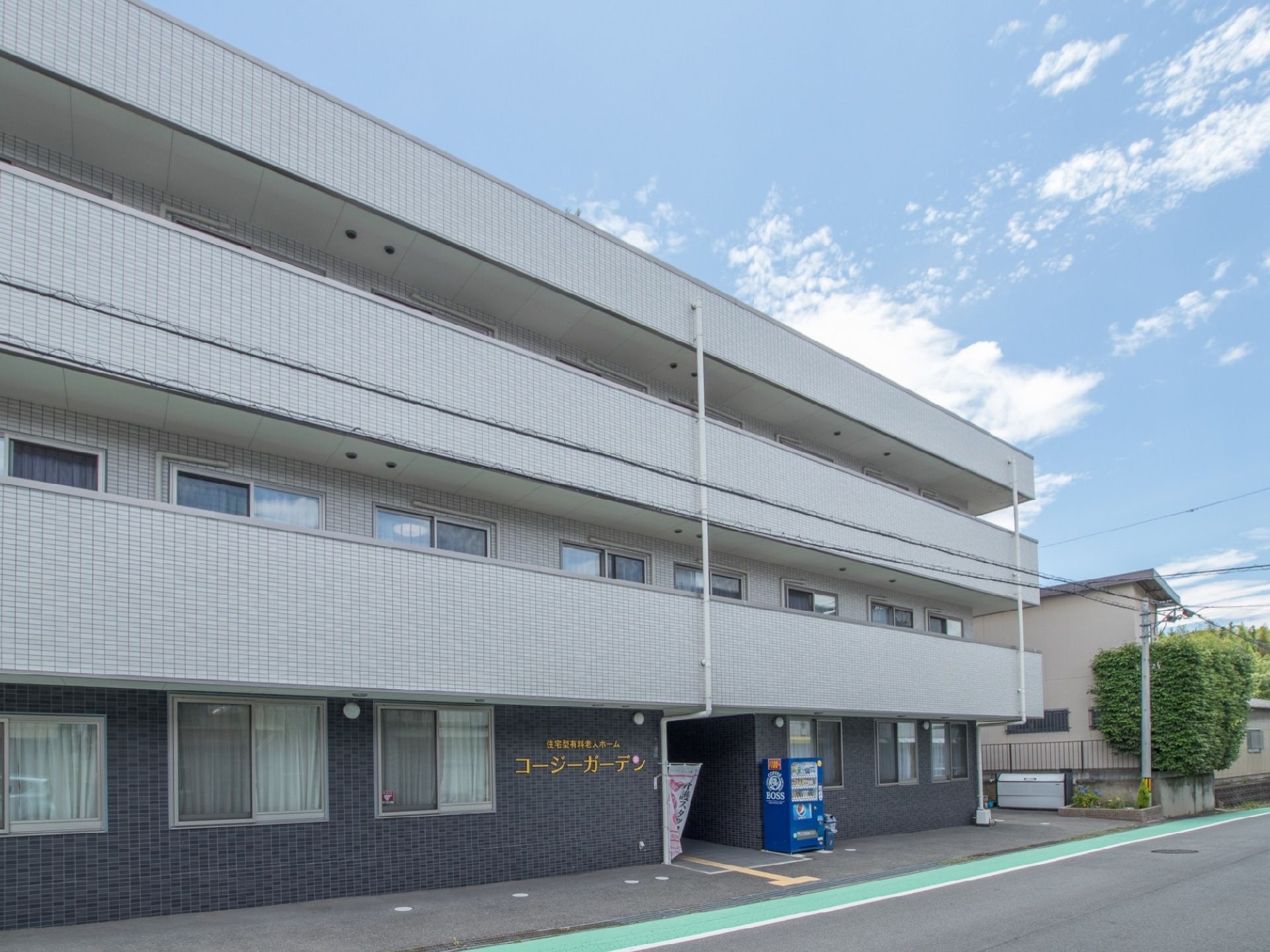 一階部分は黒、二階以上はグレーのタイル張りになった3階建ての老人ホーム。道路から施設入口まで段差のないバリアフリー仕様になっている。