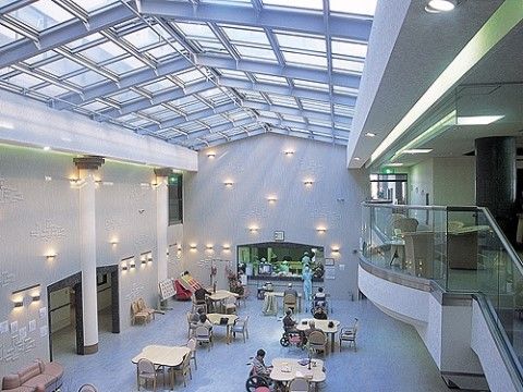 天井がガラス張りのため、太陽光が差し込む明るい空間である。奥のステージではイベントを行っており、入居者様がくつろぎながらご覧になっている。