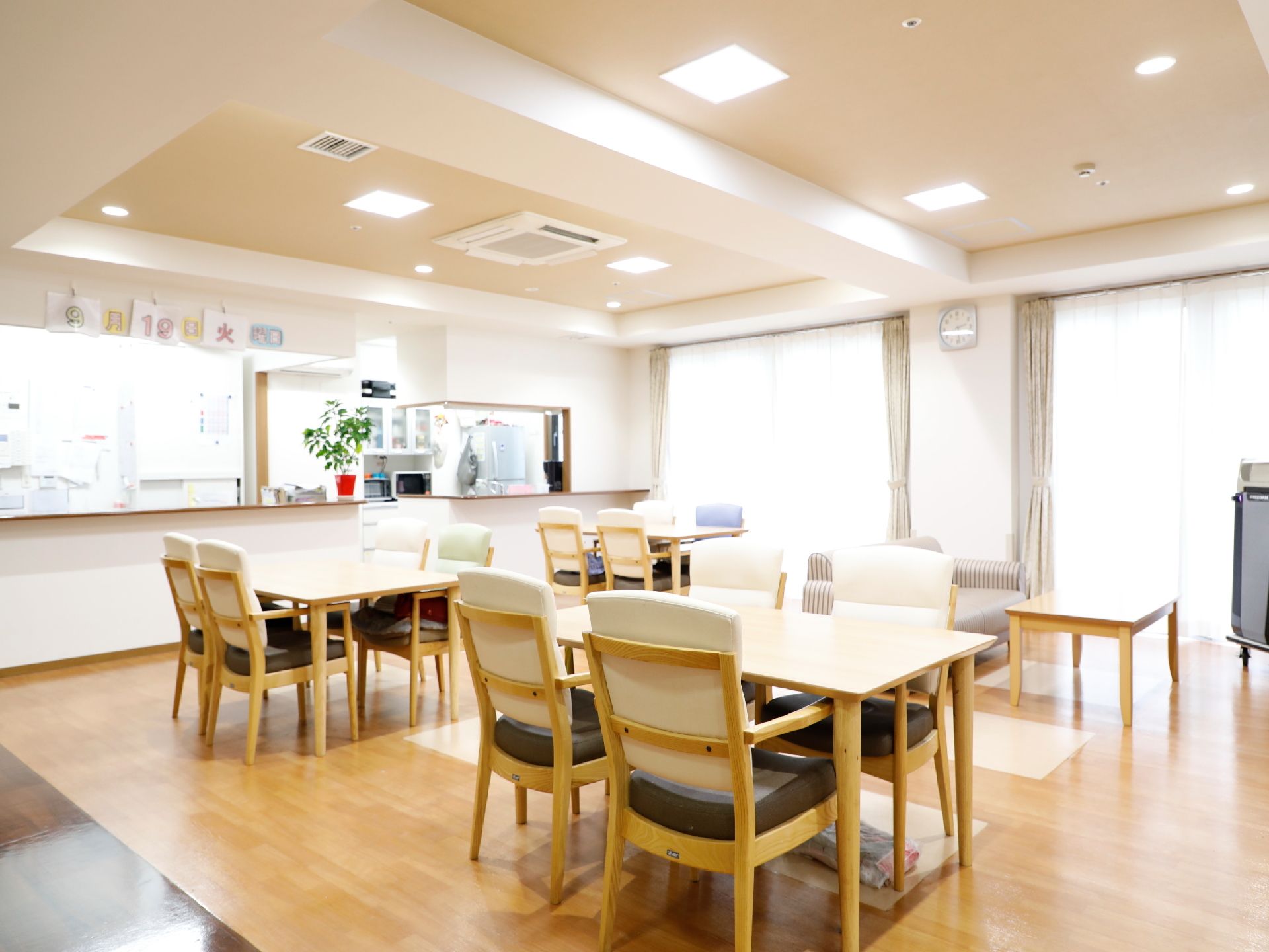 四人使用のテーブルと椅子、奥にはソファーが置かれている。奥のカウンターには鉢植えが置かれ、さらに奥はキッチンになっている。