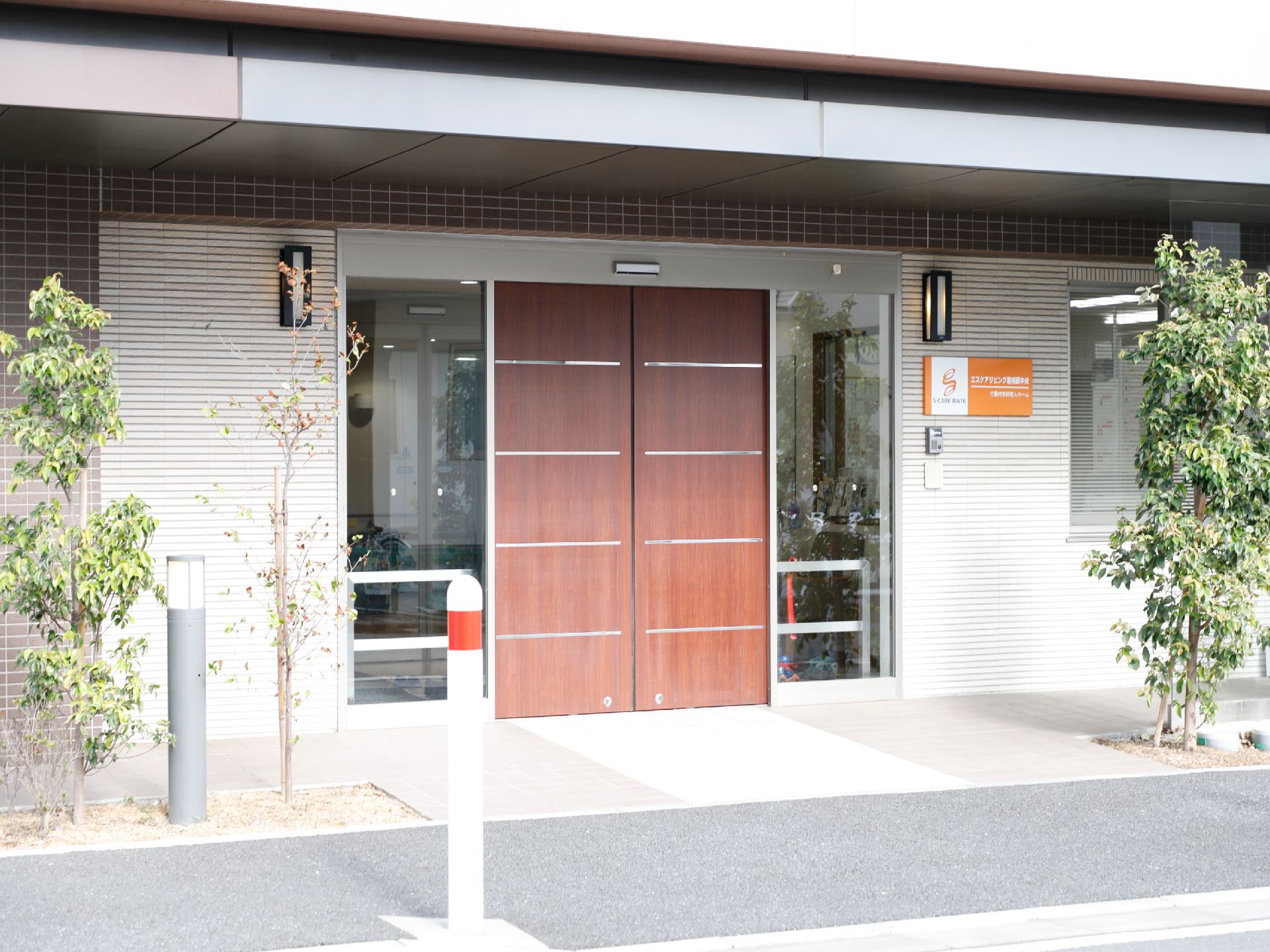 玄関はガラスと木目の自動ドアがあり照明も付いている。入り口の脇には木が植えてある。歩道から段差がなく入りやすい。