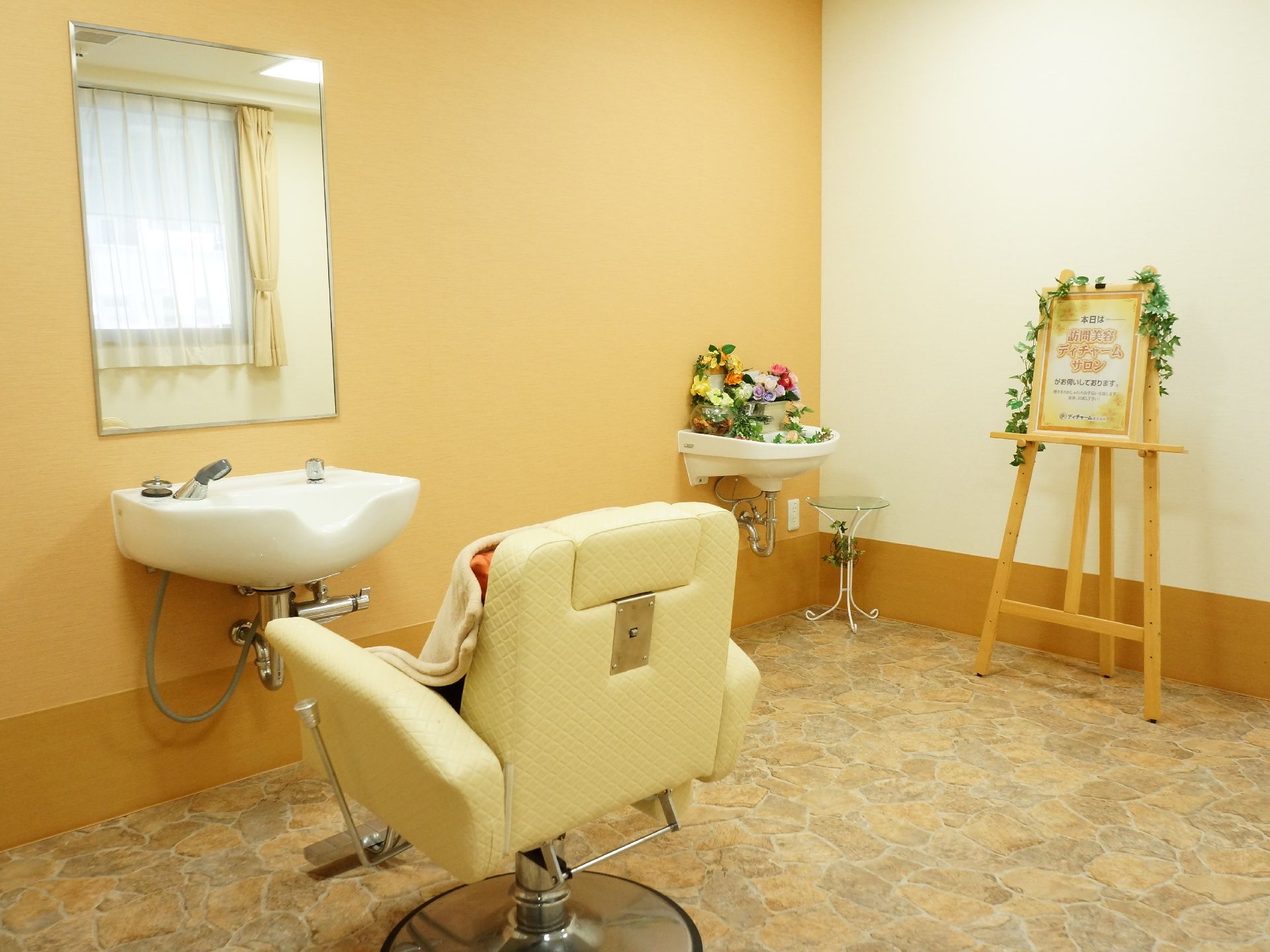 部屋の奥には、大きなイーゼルがあり、理美容室のイベントのお知らせパネルが乗せられている。洗面台にはたくさんの花が置かれている。