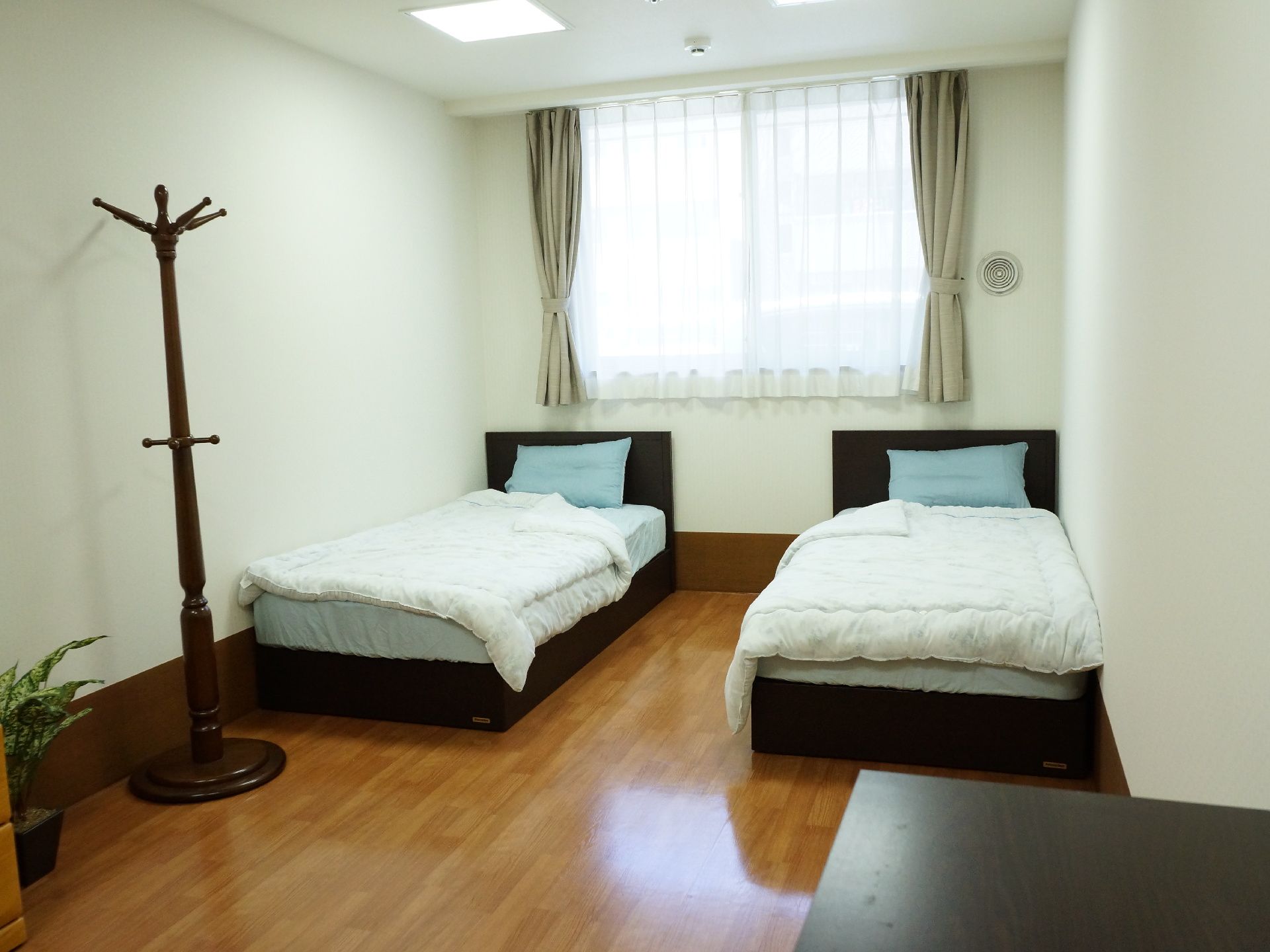 茶系のフローリングで、とても落ち着いている。部屋は窓も広くて明るい。シングルベッドが2個あり、小物はチェストに入り、洋服はポールハンガーへ。