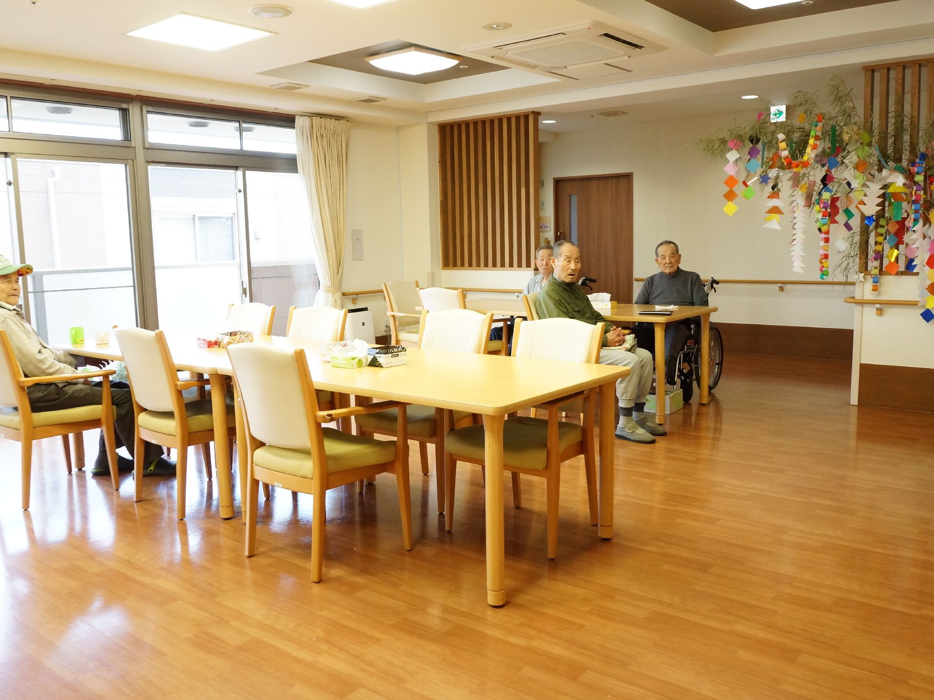 長いテーブルが2列に椅子が並んでたくさんの方が座ってテレビを見たり、くつろげる。大きな窓から光が入って明るい。