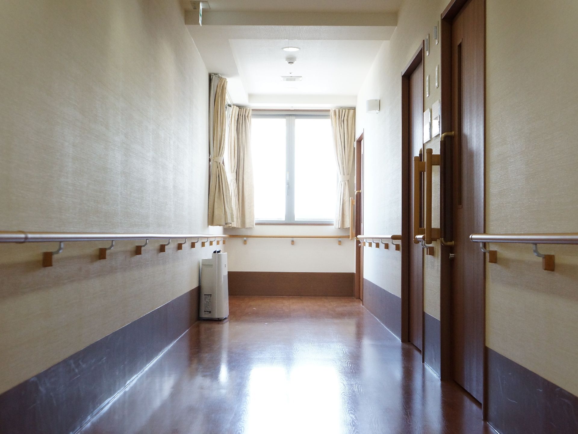 濃い色の木目の廊下や扉は落ち着いた印象を与えてくれる。廊下突き当りの窓は小さいながらも光が入り込んで明るい。