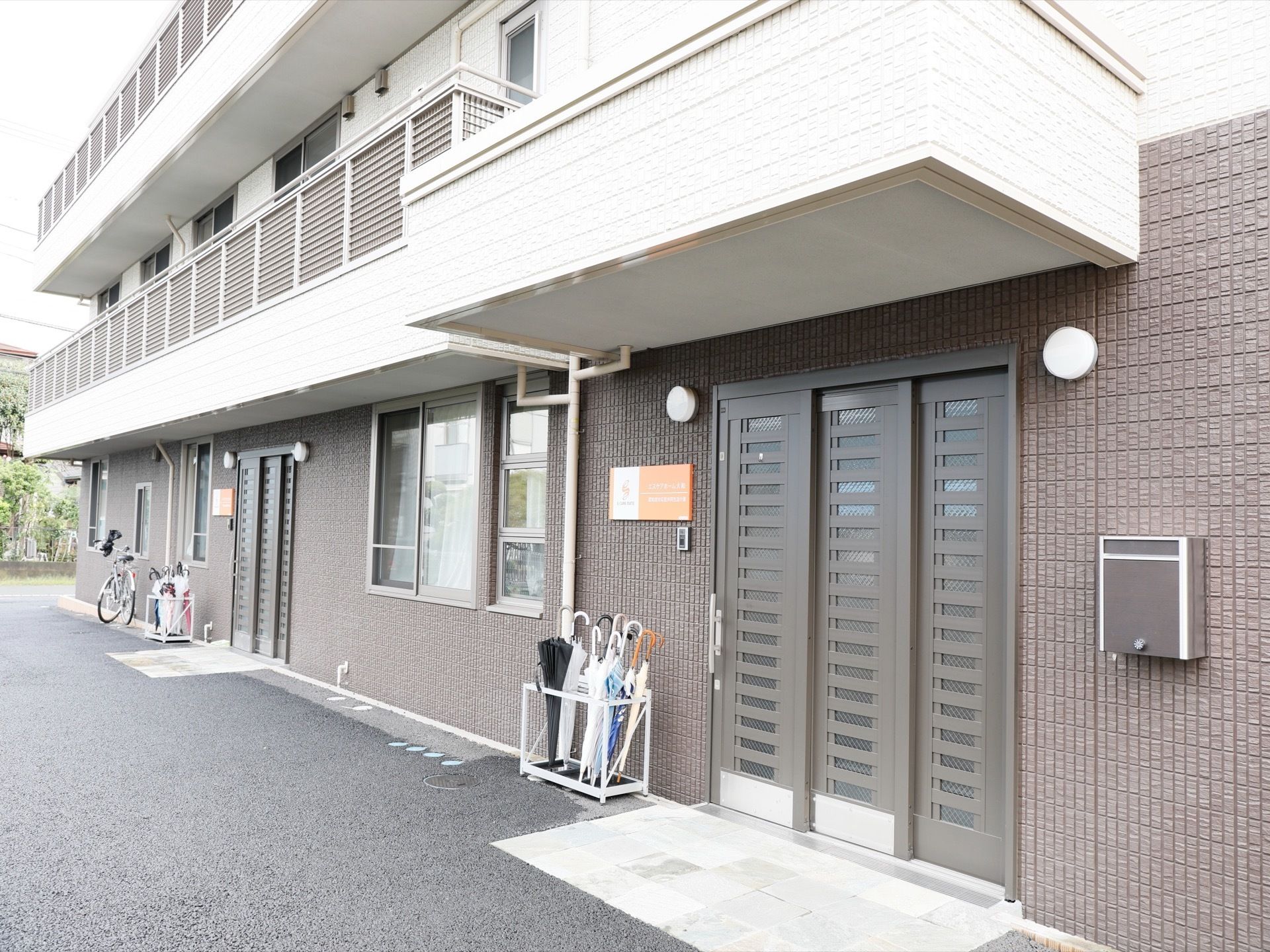 施設の建物は、上階に仕切りのない、ひと続きのベランダがある。１階の入り口前にも、ベランダがあるので屋根の代わりとなる。