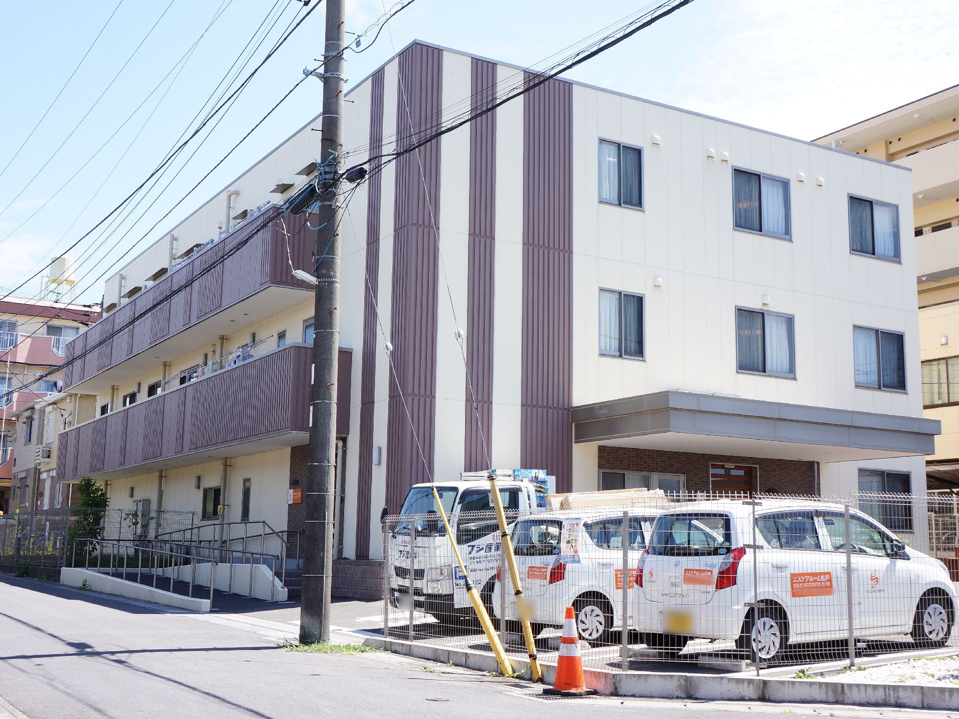 道路に面した住宅地に立地しているベージュとダークブランの外壁がおしゃれな雰囲気の3階建ての施設の概観。