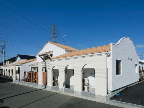 白い外壁とオレンジ屋根の、チャペルのようなおしゃれな平屋の建物。施設前はアスファルトで平坦に舗装されている。