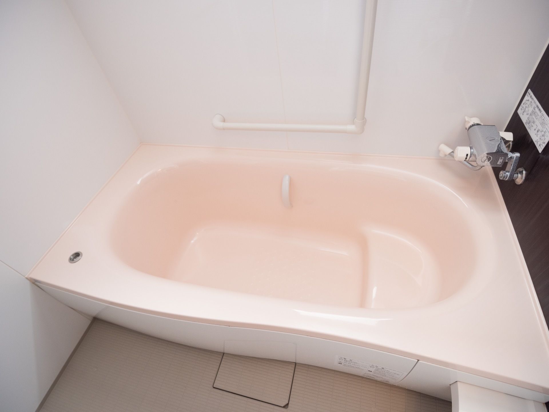 白い壁にL字型の手すりがある。ピンク色の浴槽はきれいに磨きあげられて、照明で輝いている。